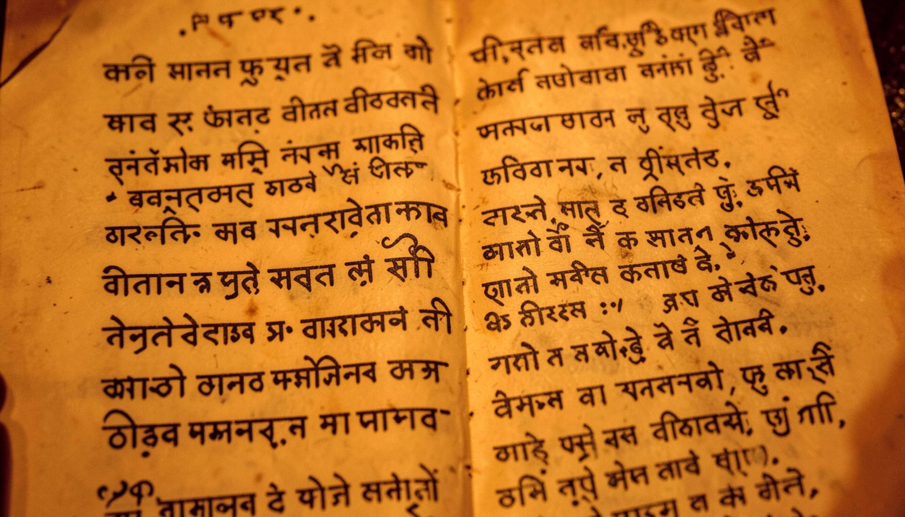Ornate Hindi script manuscript page under warm amber light, literary heritage